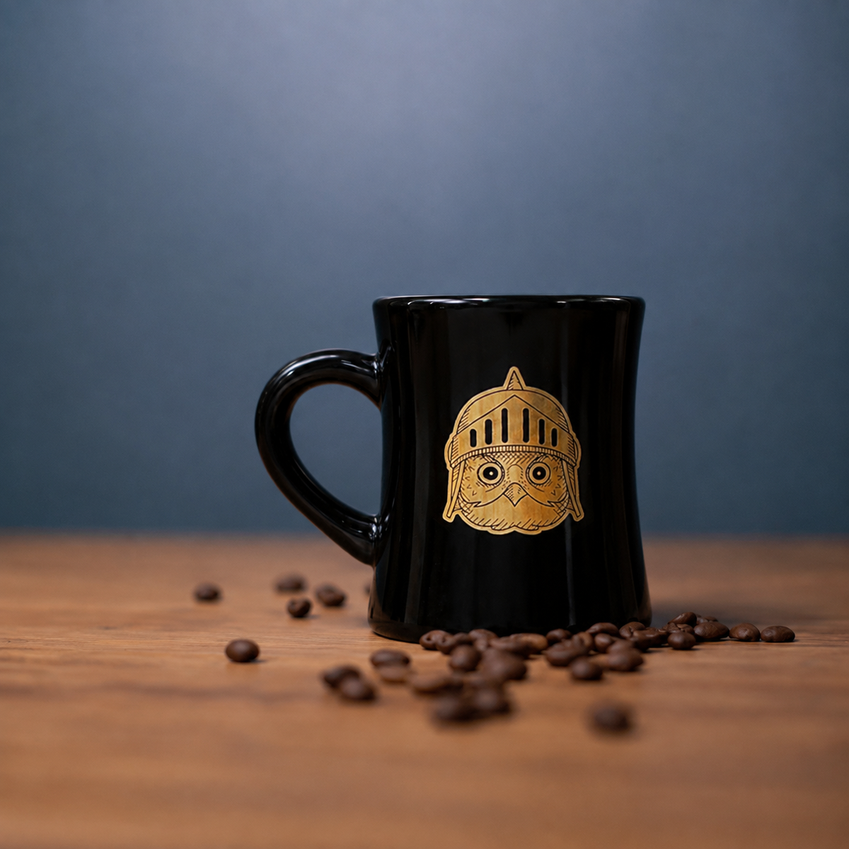 A glossy black ceramic coffee mug with a gold knight helmet design, set on a wooden surface with scattered coffee beans against a dark blue-gray background.