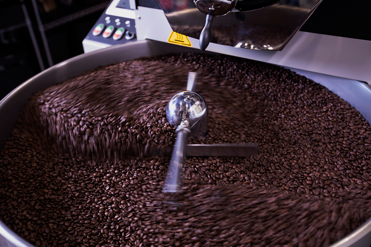 Roasted coffee beans cooling in a large metal cooling tray with a central metal agitator, captured in a close-up action shot.