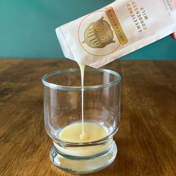 A Condensed Milk Single packet pouring condensed milk into a short glass.