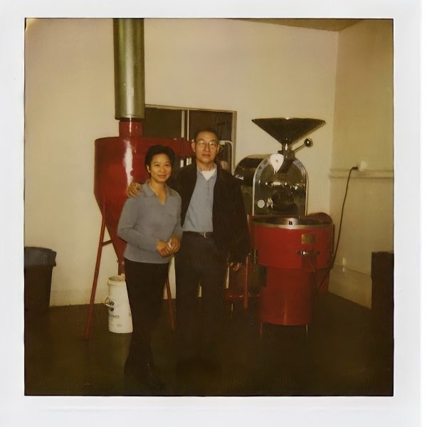 Mother and father standing in front of a red coffee roasting machine.